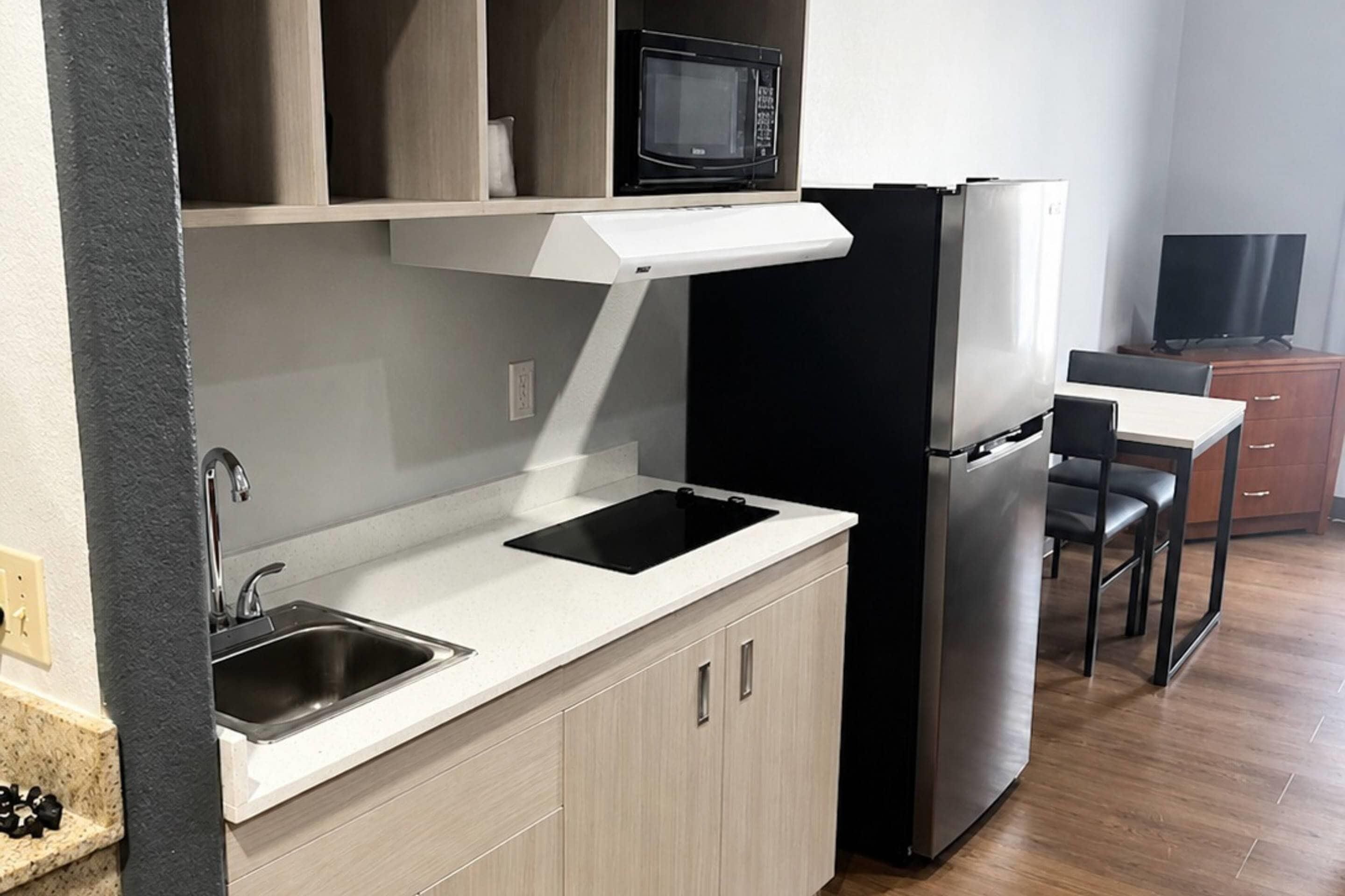 Une cuisine compacte équipée d’un four à micro-ondes, d’un réfrigérateur, d’un évier et d’un petit coin repas avec une chaise et une table.