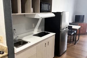 Cocina compacta con microondas, refrigerador, lavaplatos y un pequeño comedor con una silla y una mesa.
