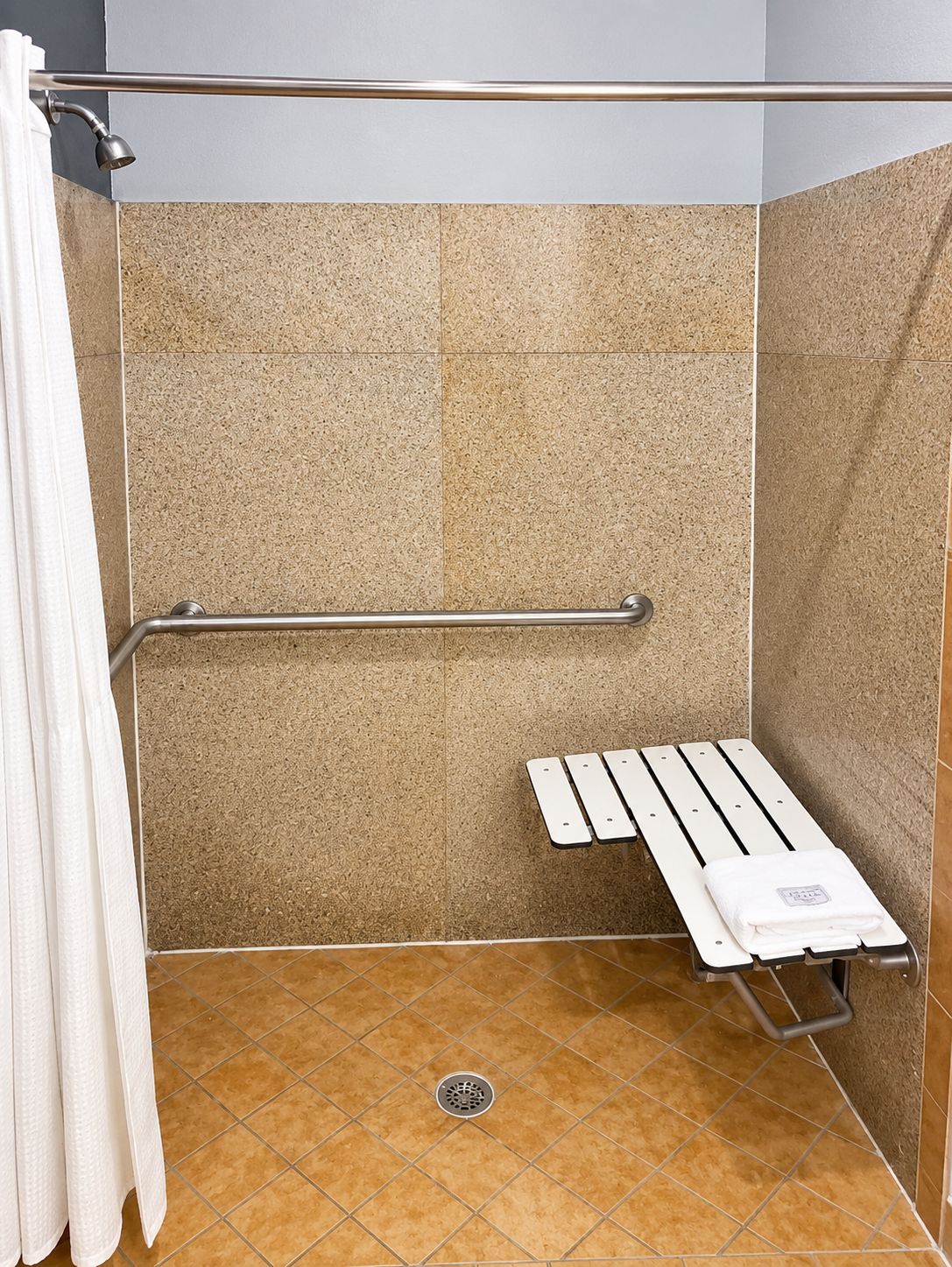 Un box de ducha con barra de apoyo, un asiento y un perchero para toallas.