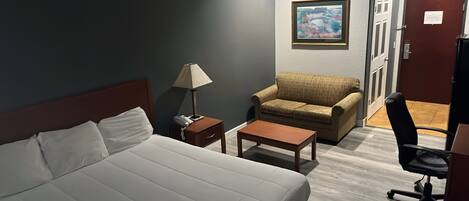 Une chambre d’hôtel avec un lit, un bureau, une chaise, une lampe et un tableau au mur.