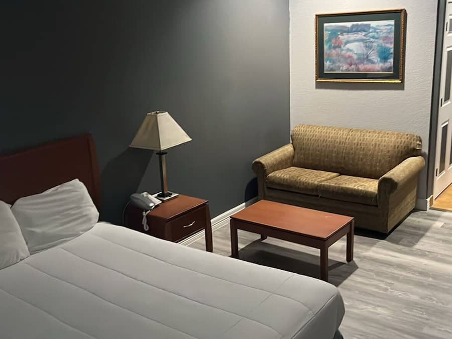 Una habitación de hotel con cama, escritorio, silla, lámpara y un cuadro en la pared.