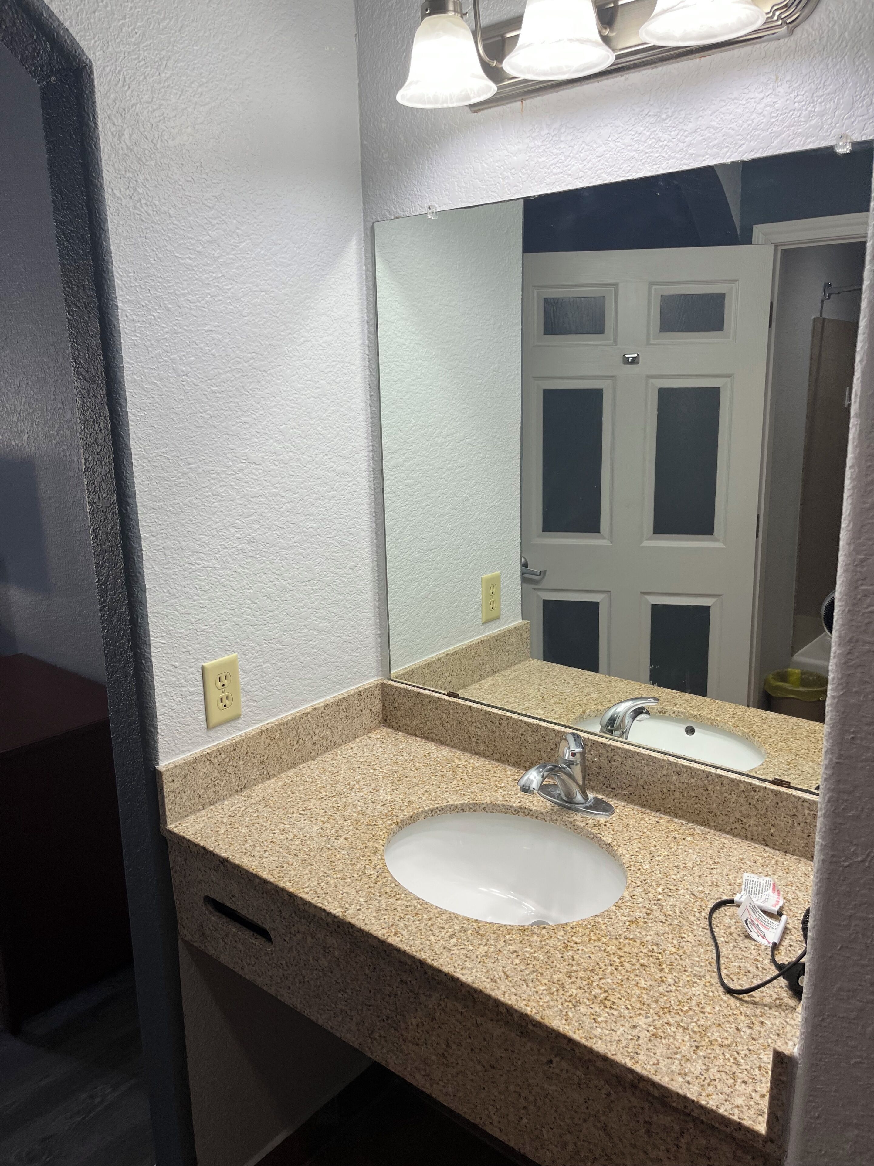 Un baño con lavamanos de encimera de granito, un espejo y una puerta al fondo.