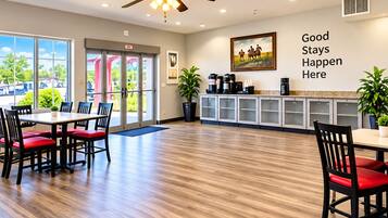 A hotel lobby with a dining area, a ceiling fan, a coffee station, and a wall with a motivational quote.