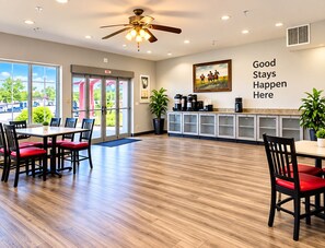 A hotel lobby with a dining area, a ceiling fan, a coffee station, and a wall with a motivational quote. - Suburban Studios Clute - Lake Jackson (Clute)