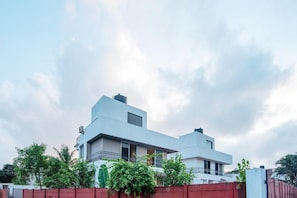 A modern two-story house with a flat roof, large windows, and a balcony.