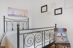 Een bed met een metalen hoofdeinde, een schilderij van zeilboten aan de muur en een ingelijste foto van een vuurtoren.