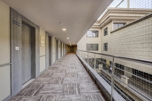 A corridor with a herringbone-patterned floor, metal railings, and a view of a building with multiple windows.
