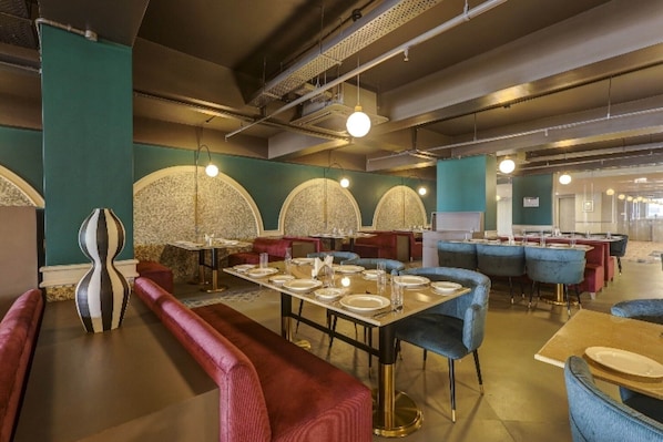 A modern restaurant with round tables, red and blue upholstered chairs, and decorative wall panels.