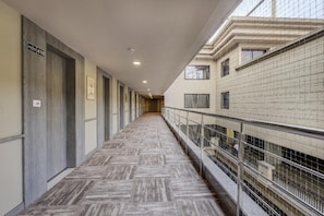 Un couloir doté d’un sol à motifs en chevrons, de rampes en métal et offrant une vue sur un immeuble avec de nombreuses fenêtres et des balcons.