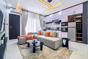 Ein modernes Wohnzimmer mit einer Couch, einem Couchtisch und einer Küchenzeile mit Schränken und Geräten.