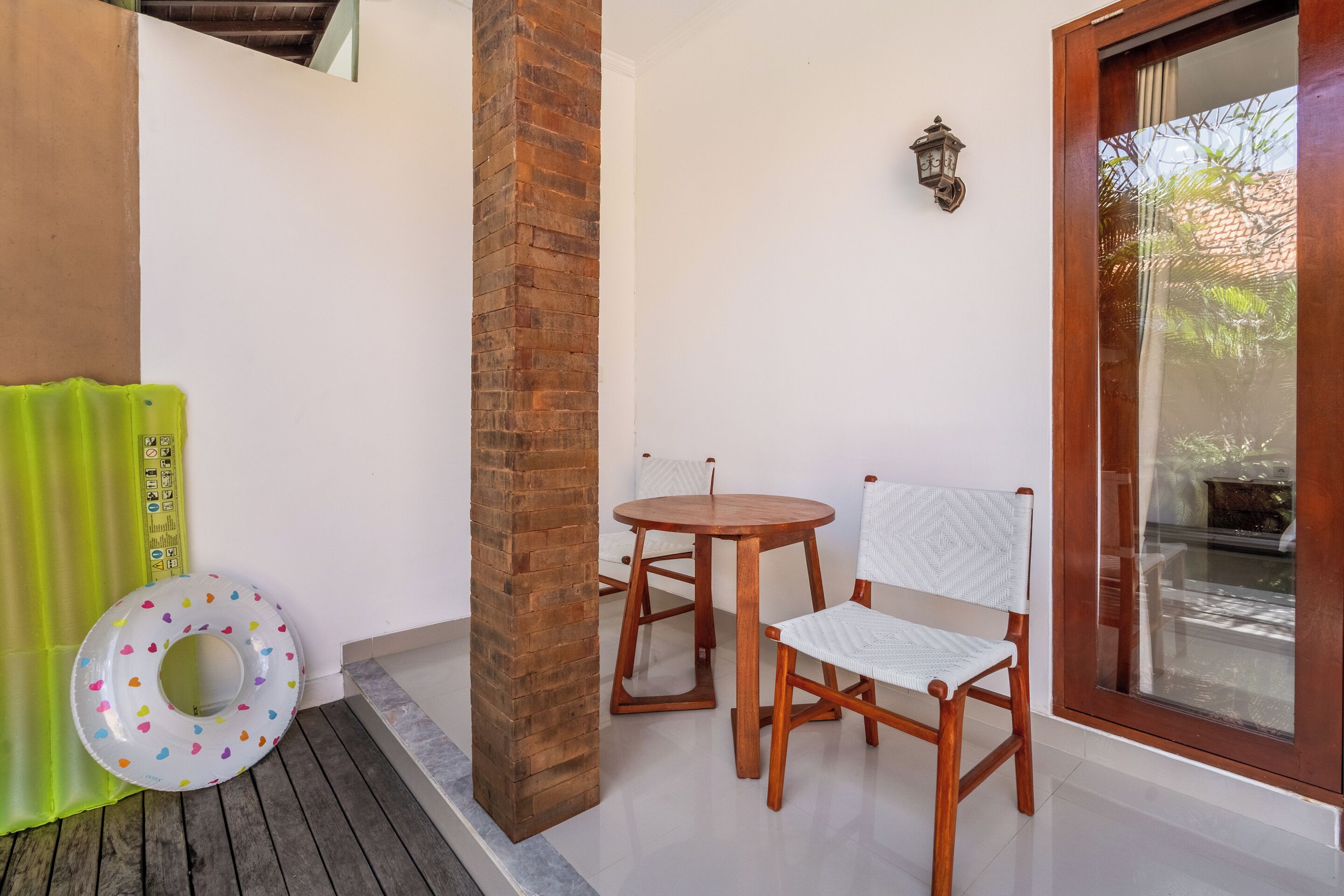 A room with a wooden pillar, a round table, two chairs, a green curtain, and a window with a view.