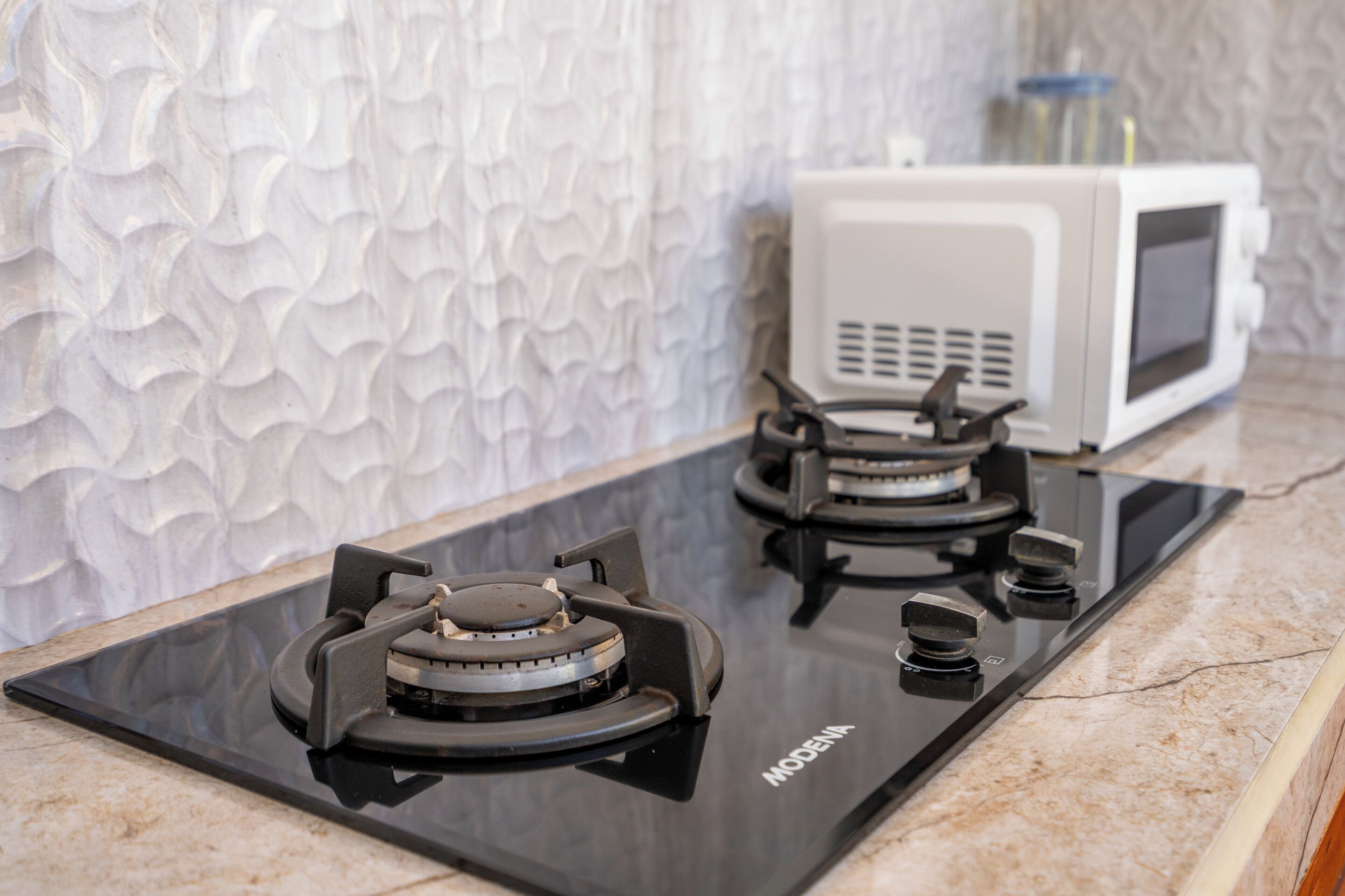 A kitchen with a black stovetop, a white microwave, and a textured wall.