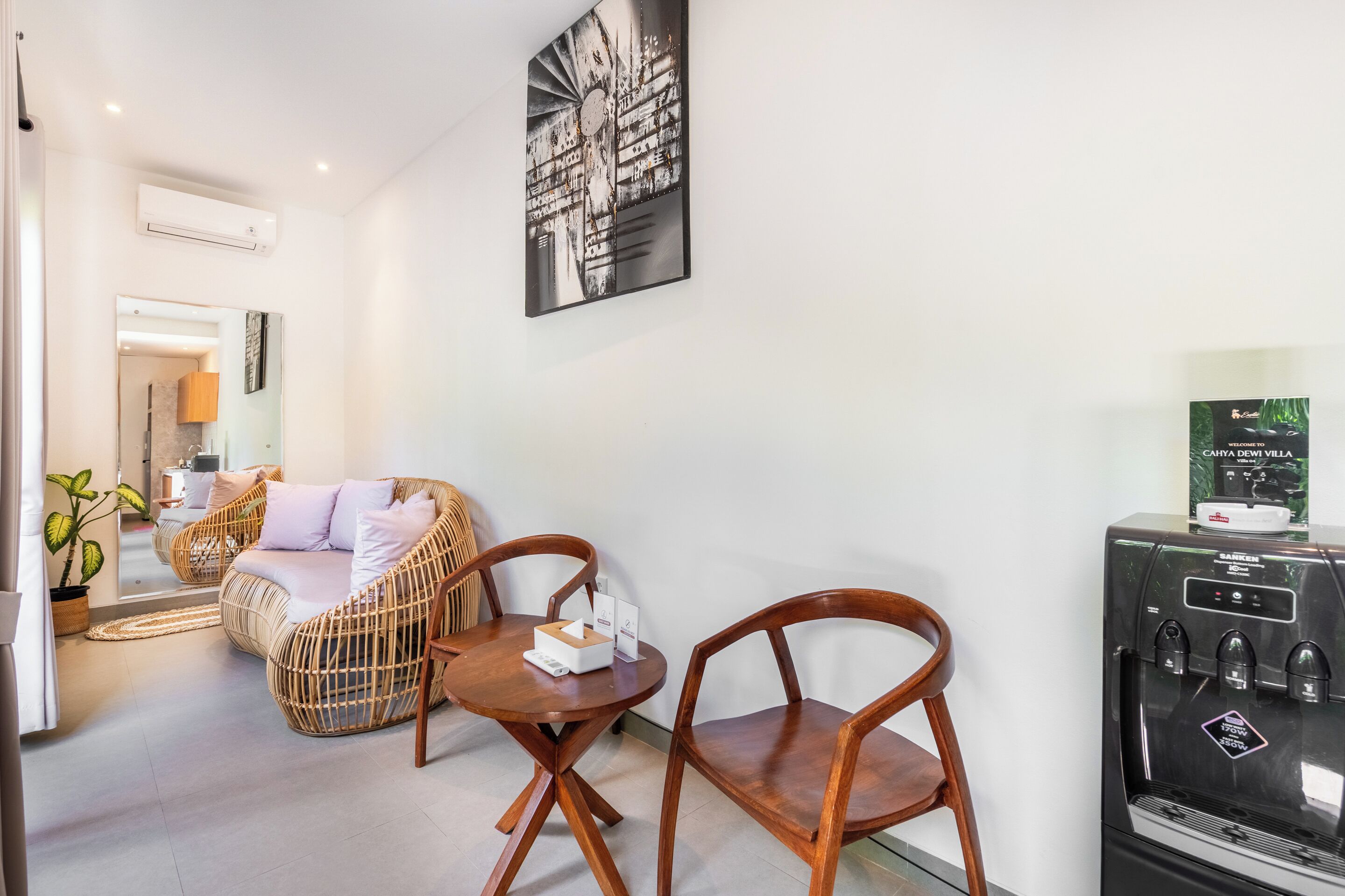 A modern room with a sofa, two wooden chairs, a small table, a water dispenser, and a mirror on the wall.