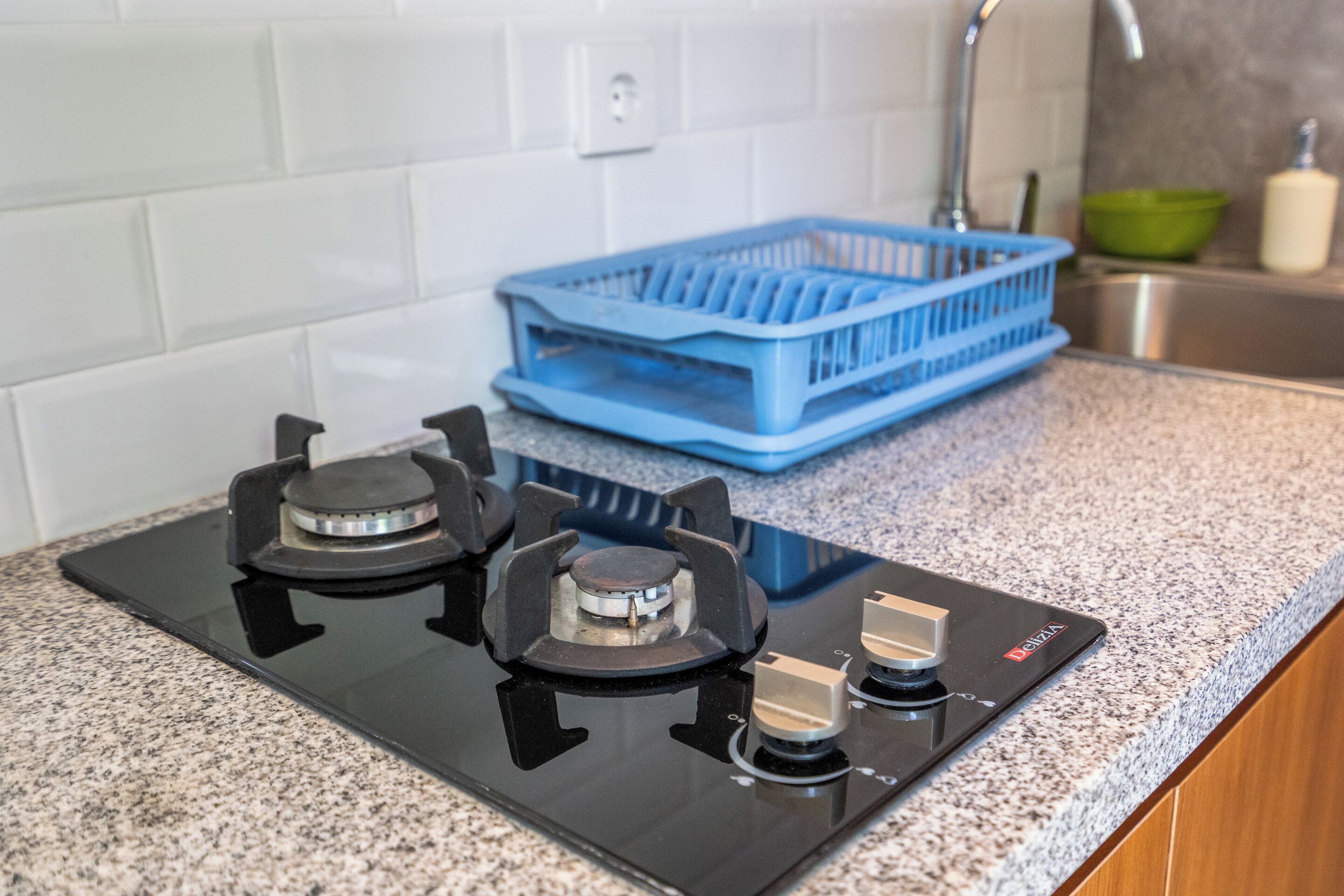 A kitchen with a black stove, a blue dish rack, and a stainless steel sink.