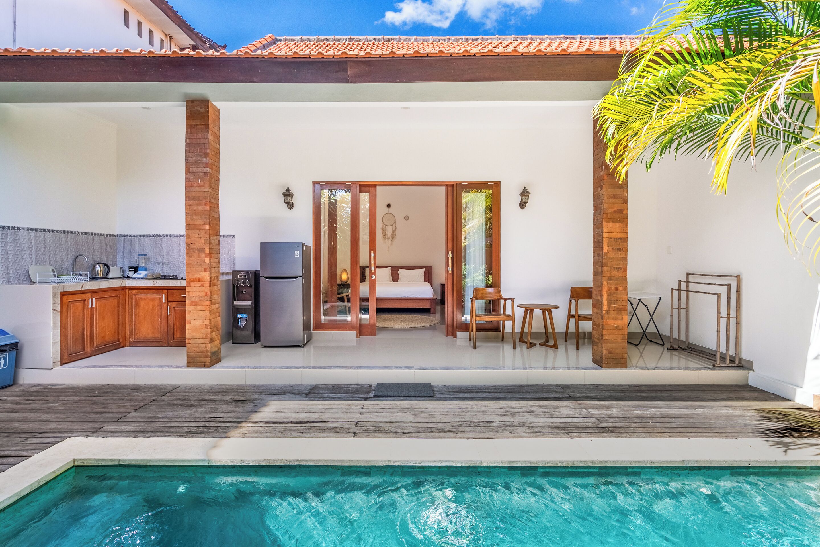 Vue sur une maison moderne depuis la piscine, avec une cuisine, une chambre à coucher comprenant un lit et un bureau, et un espace patio.