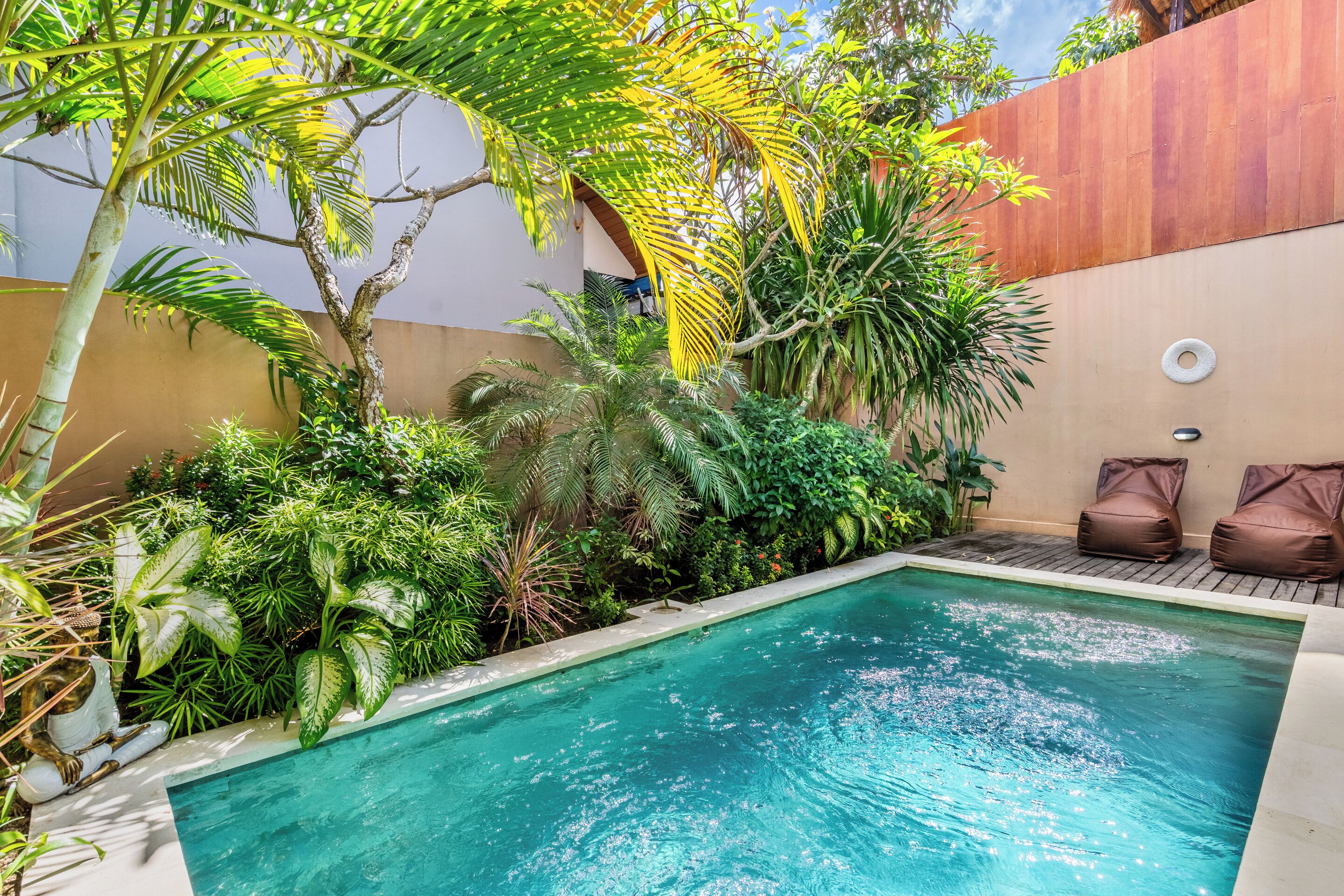 Una piscina con cubierta de madera, rodeada de exuberante follaje y una pared color beige.