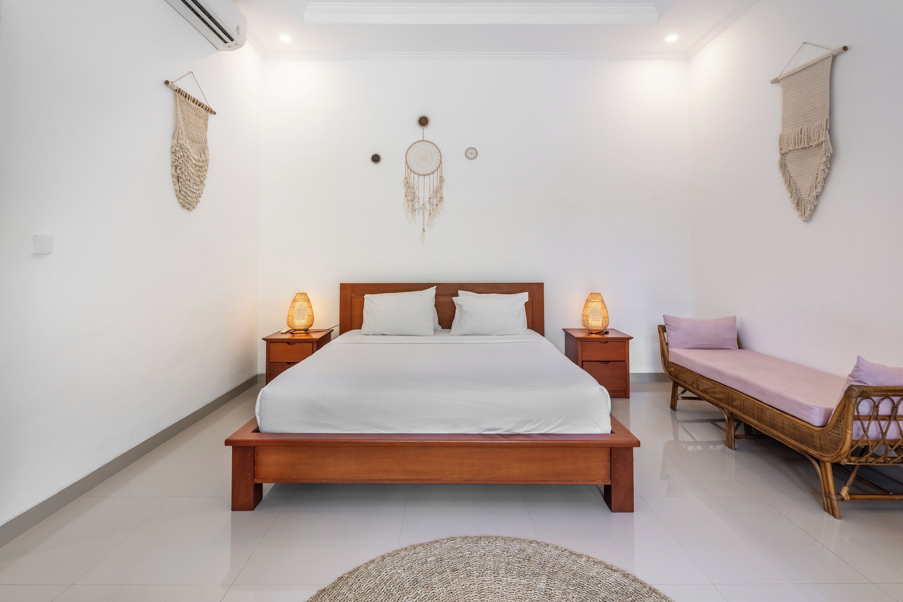 A bedroom with a wooden bed, bedside lamps, a woven rug, and a woven wall hanging.