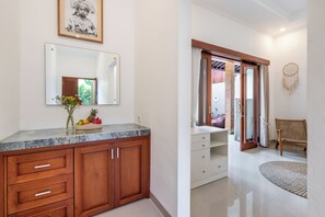 Une salle de bain avec un comptoir en marbre, des meubles en bois, un miroir et un attrape-rêves accroché au mur.