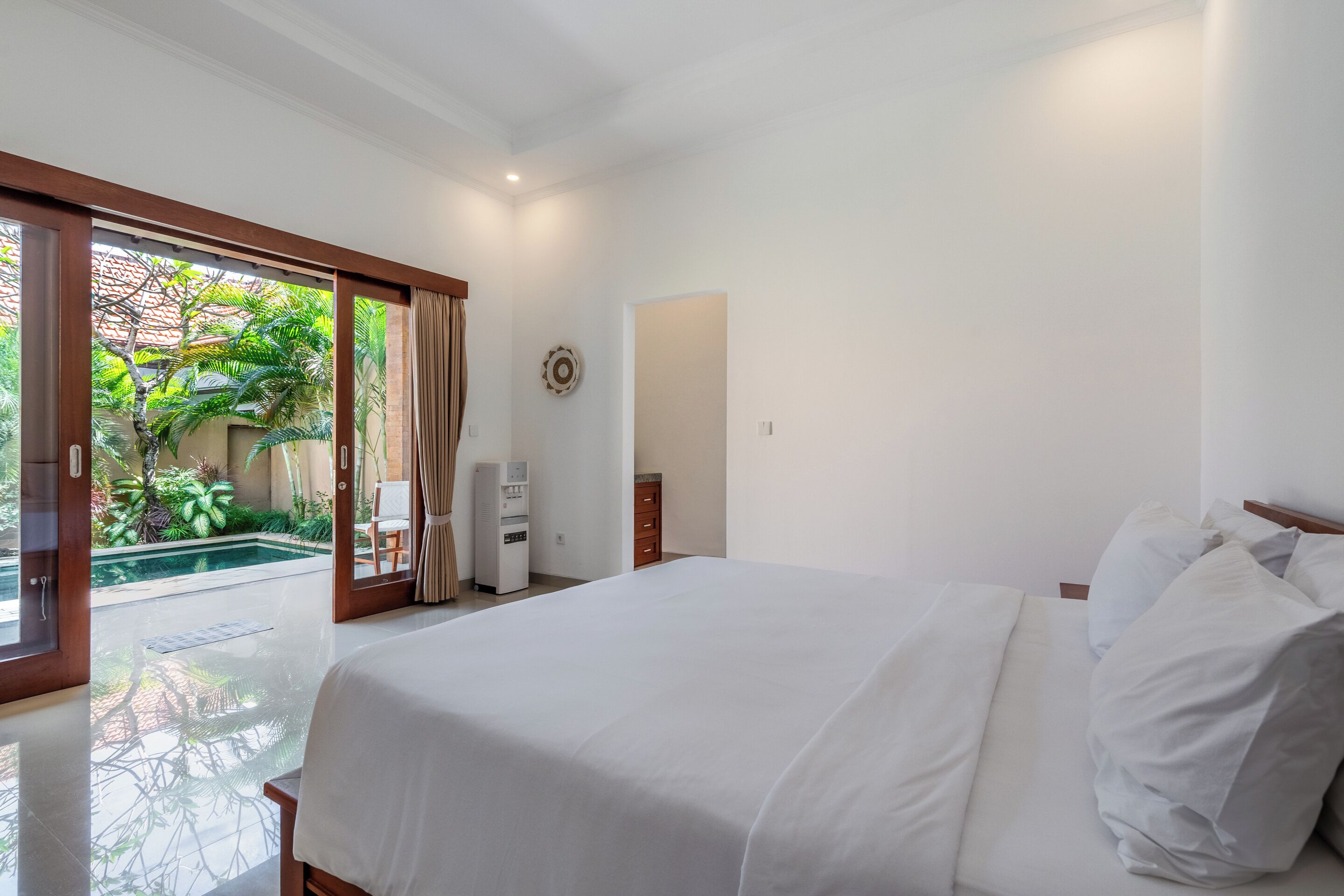 A bedroom with a large bed, a small desk, a chair, and a view of an outdoor pool area.
