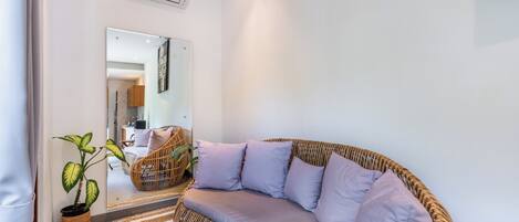 Una sala de estar moderna con un sofá curvo, una planta en maceta y un espejo que refleja la habitación.