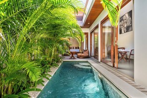 Piscina cercada por vegetação exuberante, piso de madeira e área de estar com vista para a piscina.