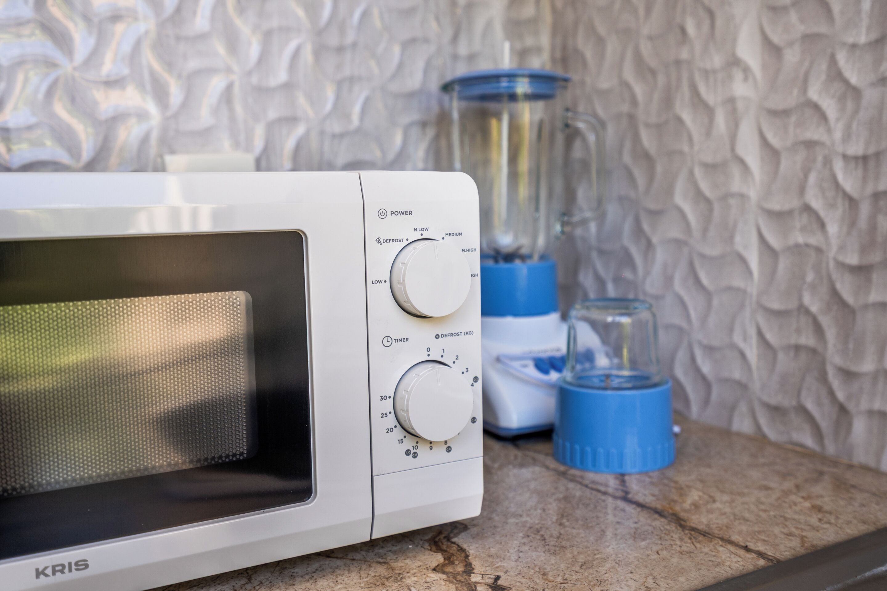 A white microwave with control knobs and a timer, placed on a countertop with a textured wall in the background.