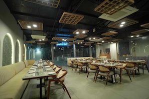 A restaurant with long tables and booths, wooden ceiling panels, and a view through large windows.
