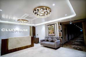 A hotel reception area with a reception desk, a grey sofa, and a chandelier.
