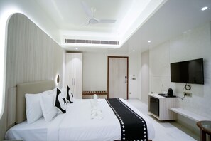 A modern hotel room with a bed, a TV, a desk, and a ceiling fan.