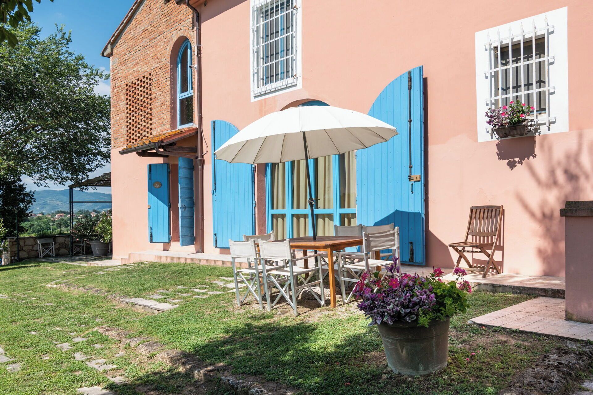 Ein Gebäude mit blauen Fensterläden, einer Terrasse mit Tisch und Stühlen und einem Blumentopf.