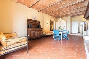 Un vaste espace de vie comprenant un canapé à motifs à carreaux, un meuble en bois, une table à manger avec des chaises bleues et un sol carrelé.