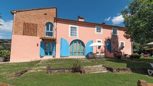Un edificio de dos pisos con fachada de ladrillo y puertas azules, rodeado de un césped cuidado y muros de piedra.