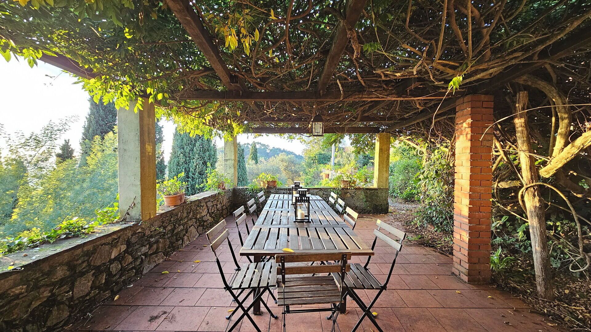 Un espace extérieur aménagé pour les repas, doté d’une pergola, de murs en pierre et offrant une vue sur un jardin luxuriant.