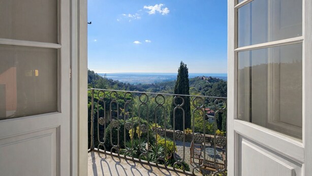 Ein Balkon mit Blick auf eine Küstenlandschaft, darunter Bäume und eine entfernte Küste.