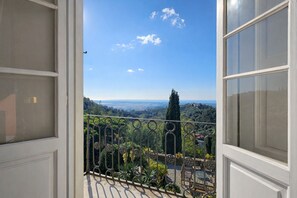 Un balcon offrant une vue sur un paysage côtier, avec des arbres et une ligne de côte lointaine.