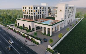 A multi-story hotel with a rooftop pool, landscaped gardens, and a road in the foreground.