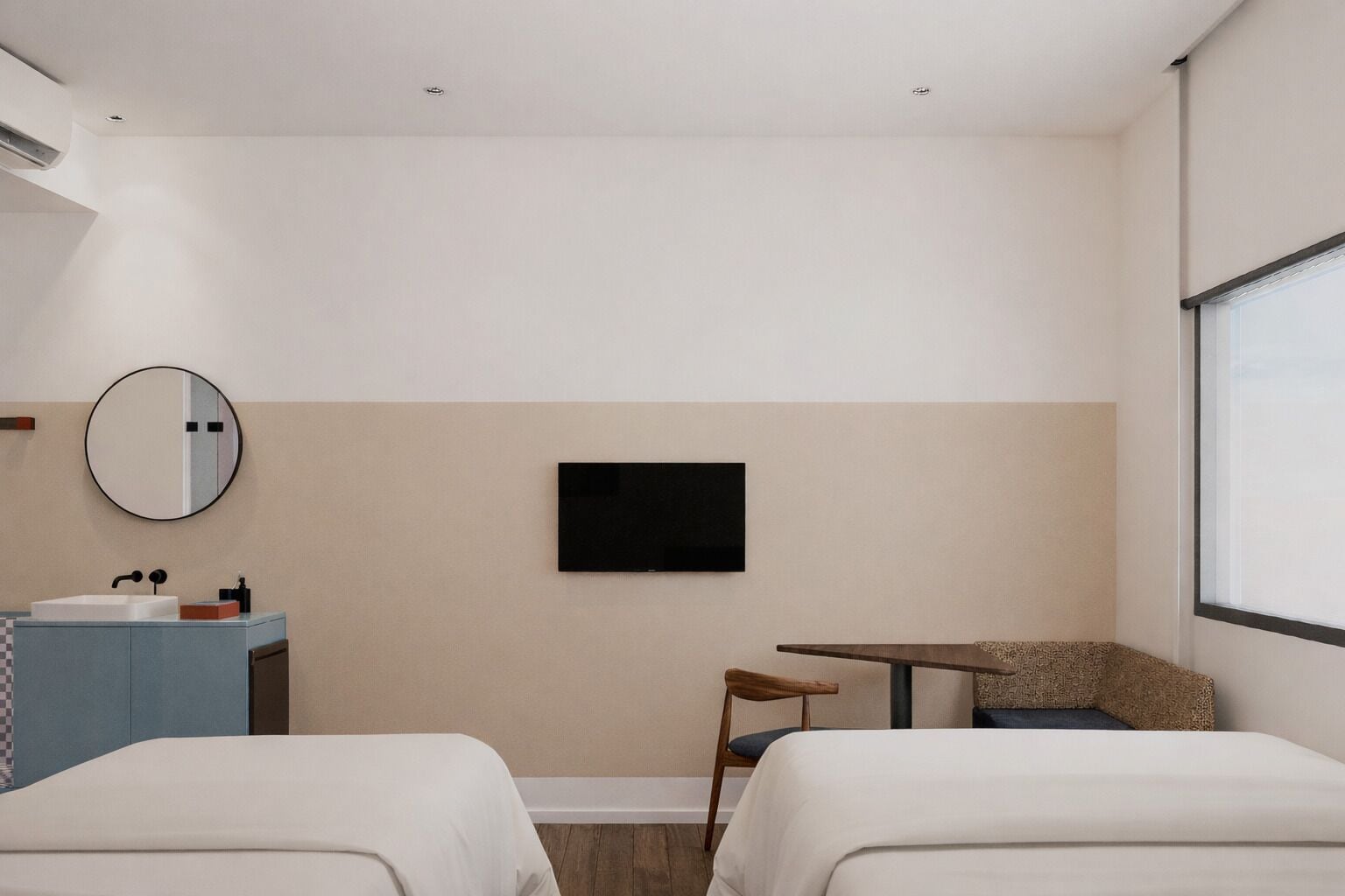 Une chambre d’hôtel avec deux lits, un téléviseur fixé au mur, une petite table, une chaise et une salle de bain avec un lavabo et un miroir.