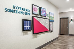 Un pasillo con un cartel que dice 'EXPERIENCE SOMETHING NEW' y una pared que exhibe diversas obras de arte enmarcadas.