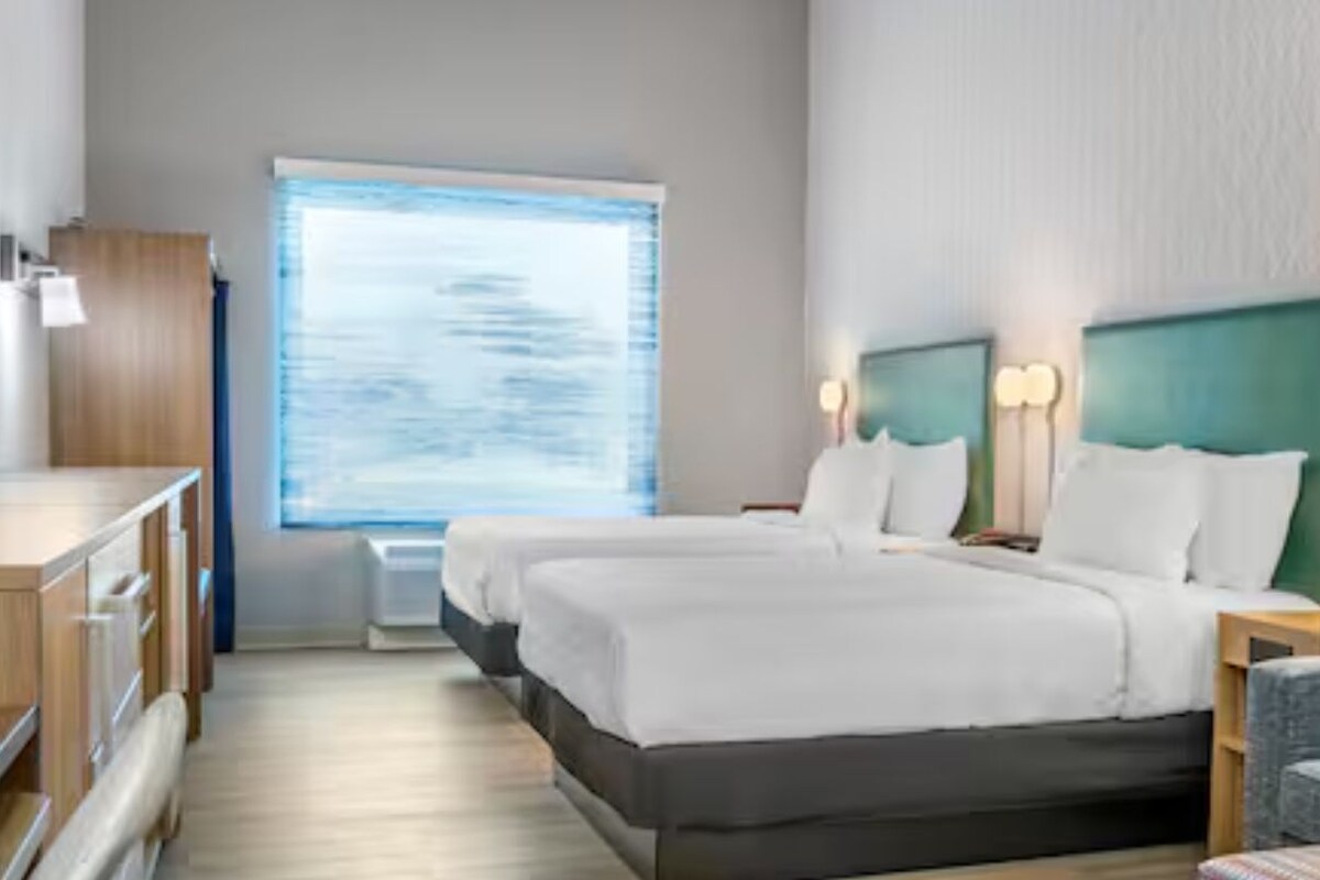 Hotellihuone, jossa on sänky, työpöytä, tuoli, ikkuna ja taulu seinällä.