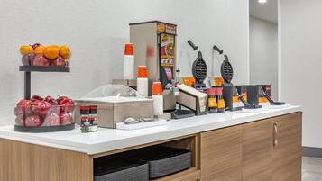 A breakfast bar with fruit, condiments, waffle makers, and disposable cups.