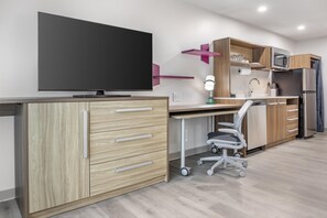 Una cocina moderna con televisor de pantalla plana, armarios de madera, microondas y refrigerador.