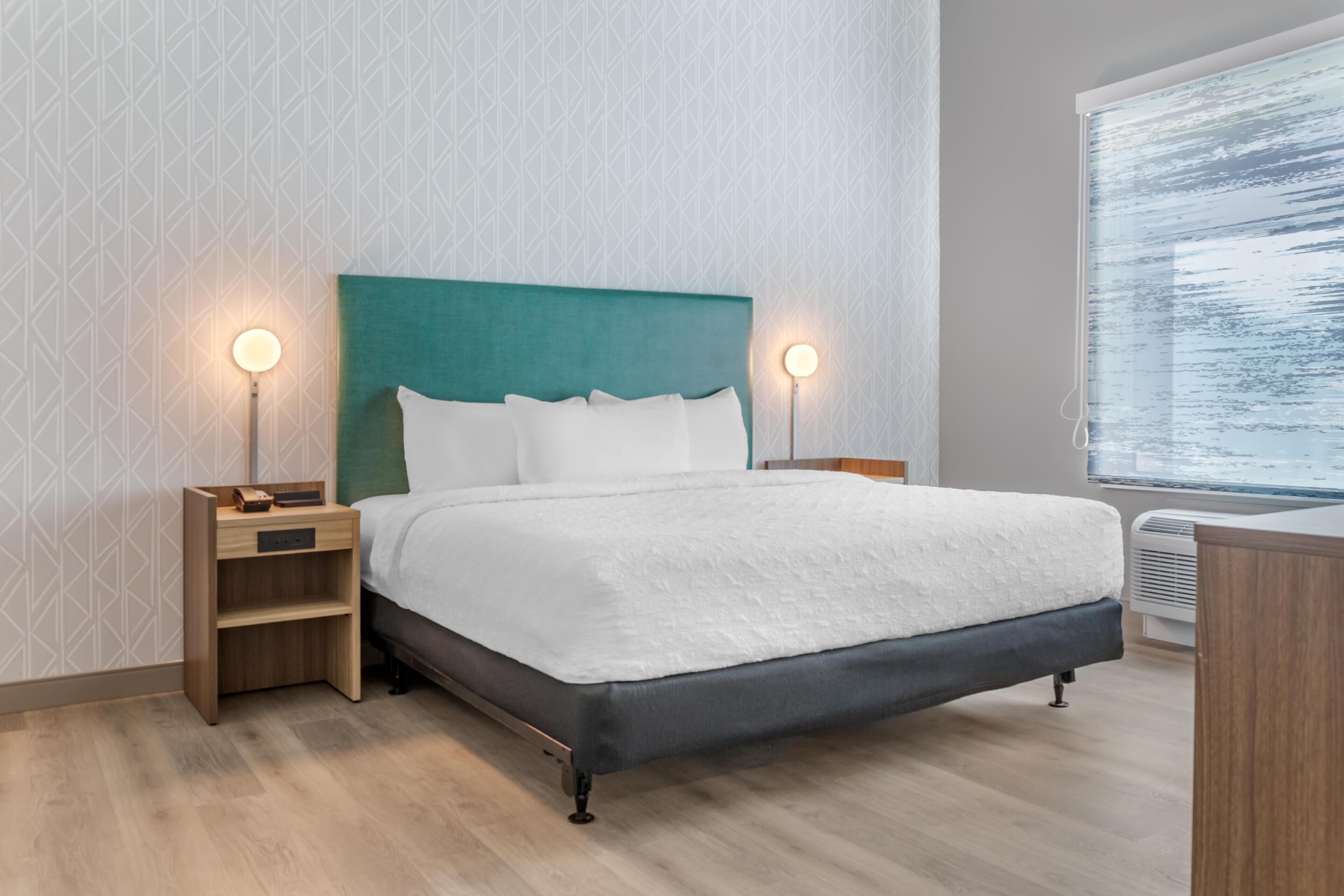 Una habitación de hotel moderna con una cama, mesitas de noche y una ventana.