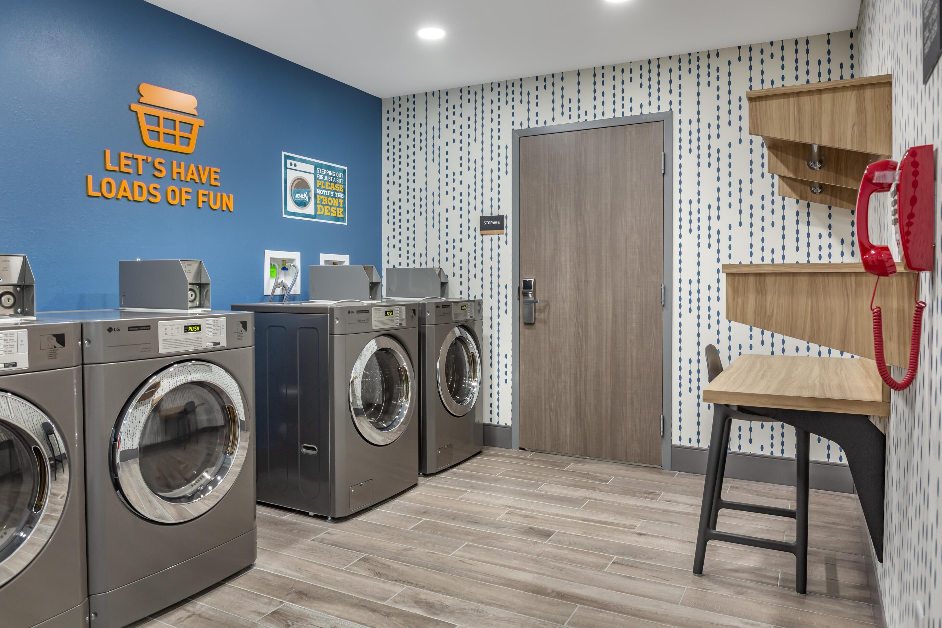 A laundry room with two LG washing machines, a wooden stool, a red telephone, and a wall-mounted sign.