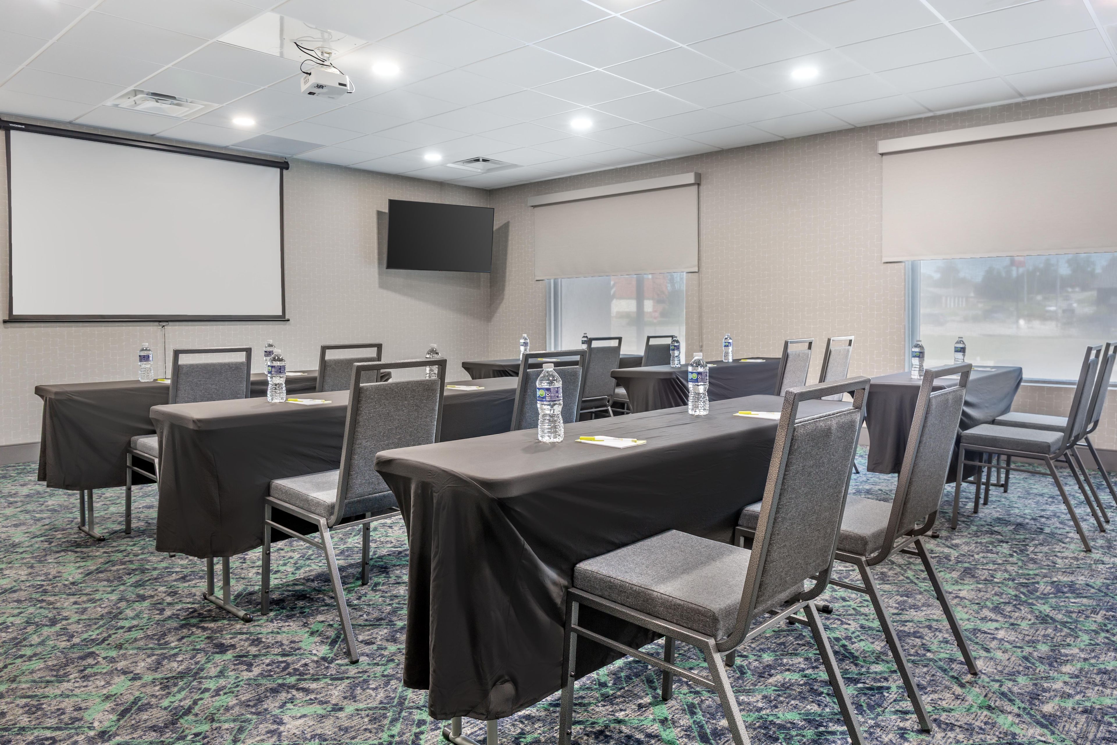 A conference room with tables, chairs, a projector screen, and a large window.