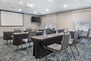 Uma sala de conferências com mesas, cadeiras, uma tela de projetor e um grande janela.