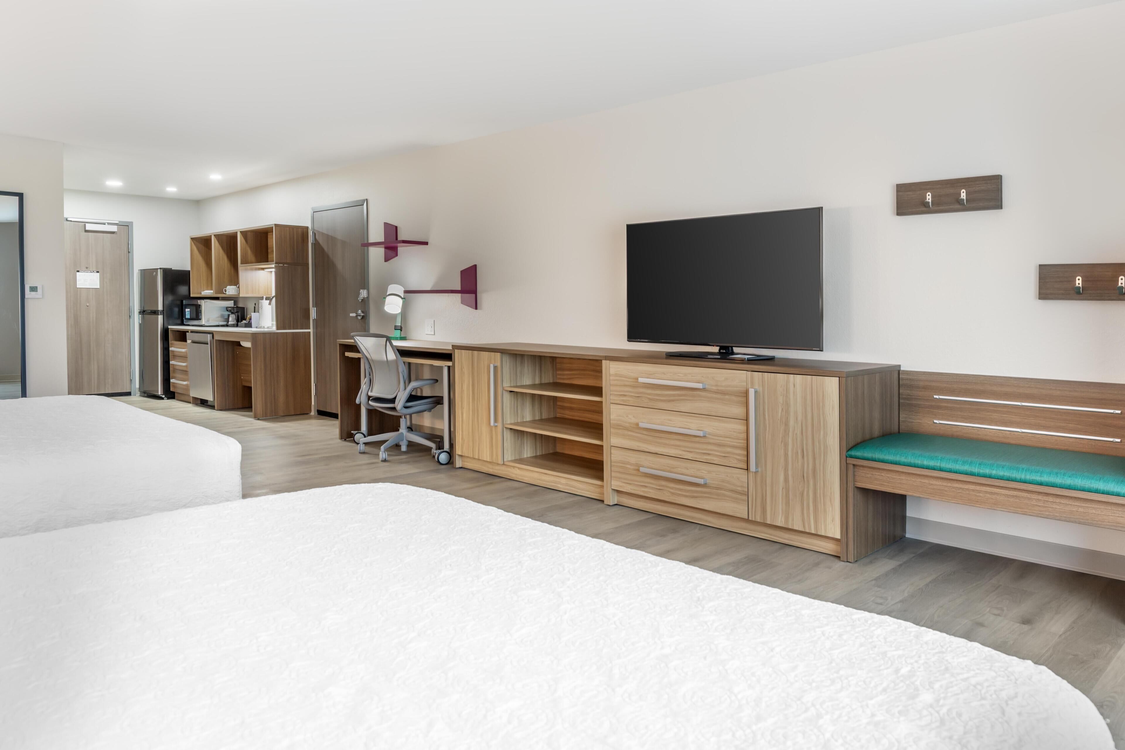 Habitación de hotel moderna con una cama grande, un escritorio con ordenador, televisión y kitchenette.