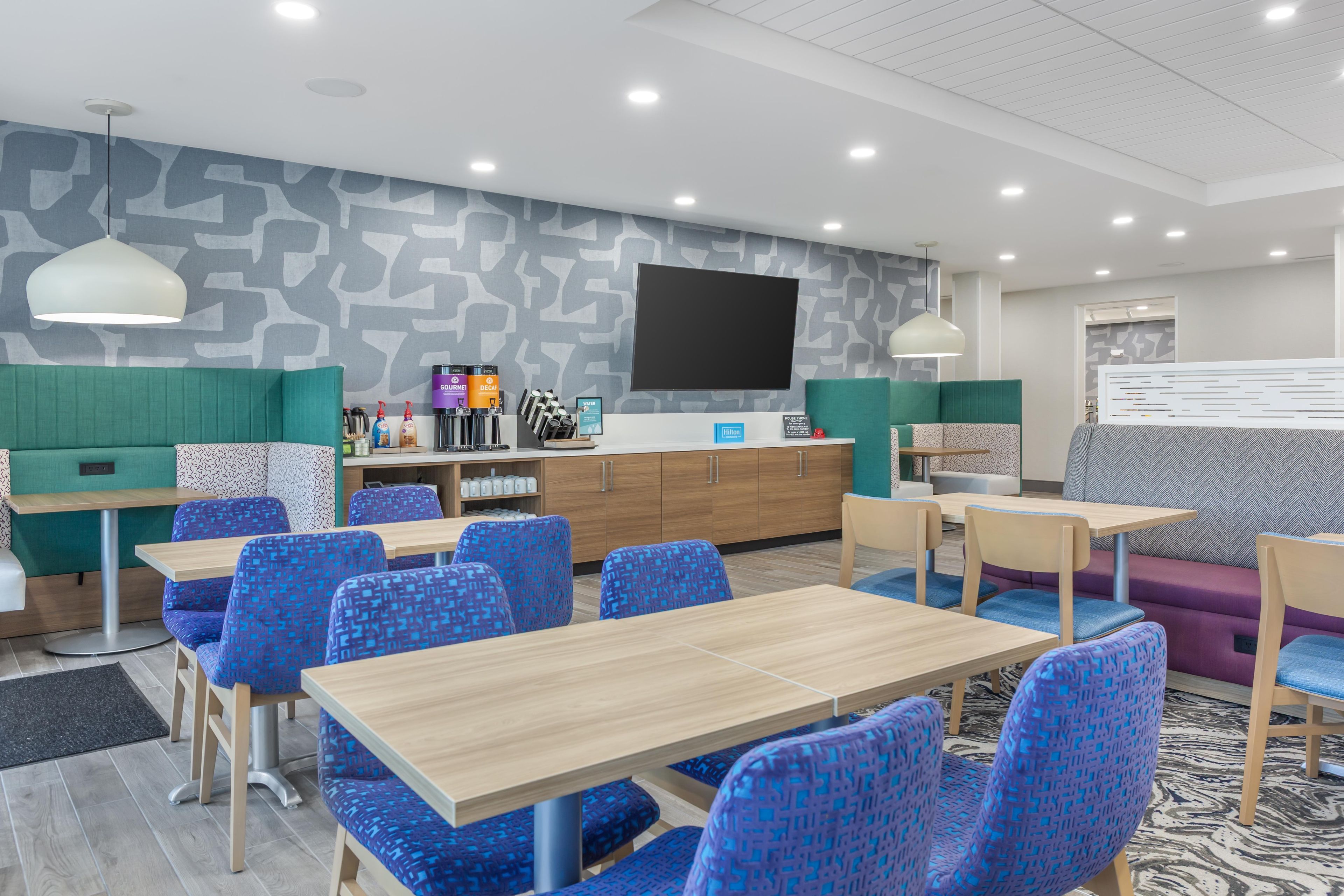 A modern hotel lobby with seating areas, a reception desk, and a large flat-screen TV.