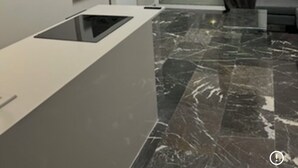 Uma sala de estar moderna com televisão de tela plana, bancada de cozinha embutida e uma grande janela com cortinas.