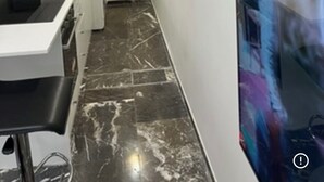 Um corredor estreito com uma pia branca, uma luminária pendente preta e um espelho refletindo uma pessoa.
