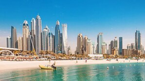 A coastal cityscape with modern skyscrapers, a sandy beach, and a boat on the water. - Settler.Homes, Breathtaking 2BR Marina, HighFloor (Dubai)